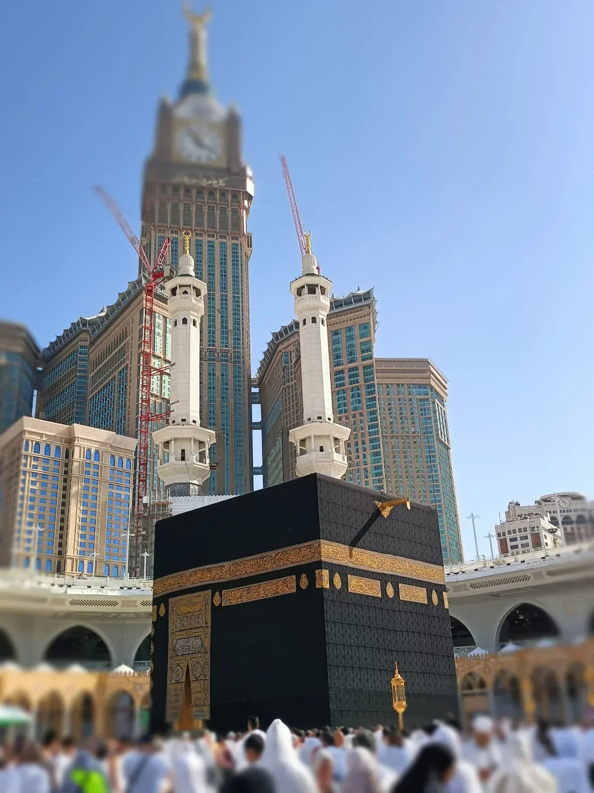 Kaaba in Mecca with the Abraj Al Bait clock tower and white minarets, pilgrims around during Umrah or Hajj