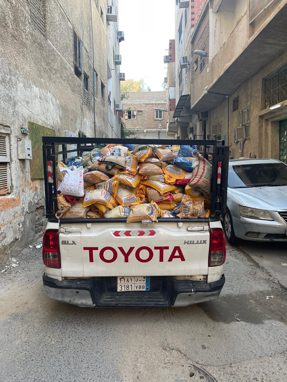White Toyota Hilux pickup truck loaded with sacks of supplies on a narrow urban street