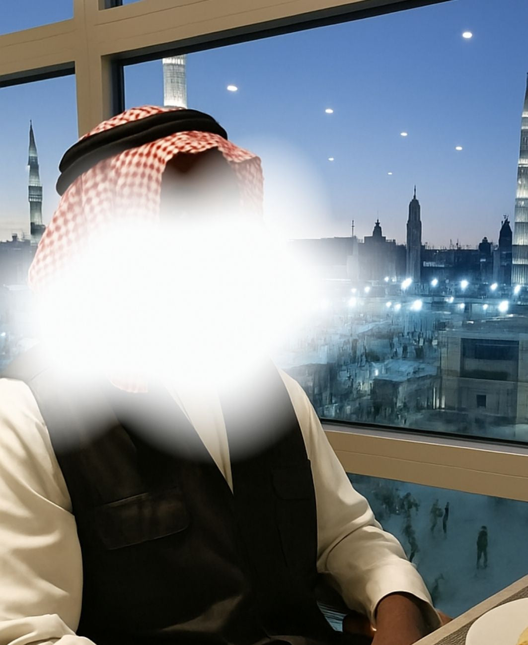 Khadim wearing a checkered headscarf looking out a window at a cityscape with illuminated buildings.